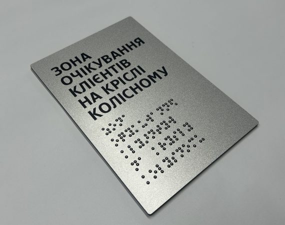 Срібляста табличка «Зона очікування клієнтів на кріслі колісному» з написом шрифтом Брайля