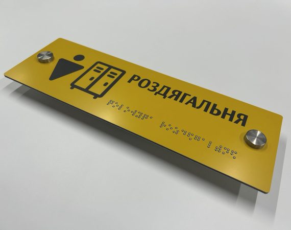 Жовта табличка «Роздягальня» з піктограмою шафок і шрифтом Брайля, сфотографована під кутом