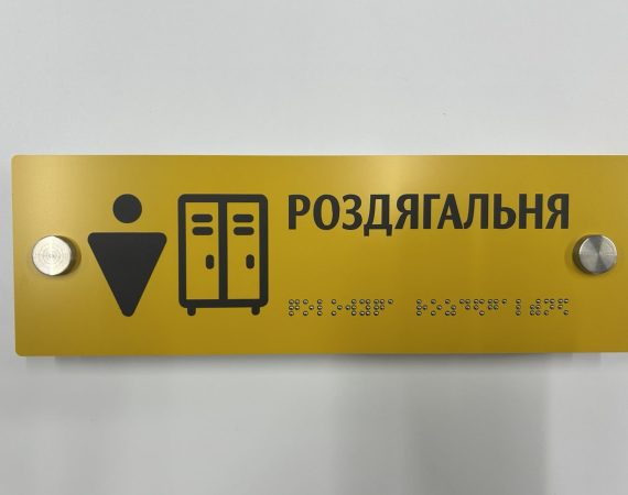 Жовта табличка «Роздягальня» з піктограмою шафок і написом шрифтом Брайля, вигляд спереду