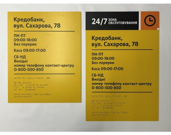 Дві жовті інформаційні таблички «Кредобанк» з адресою, графіком роботи та шрифтом Брайля