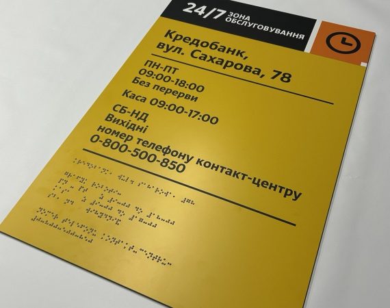 Крупний план жовтої інформаційної таблички «Кредобанк» з графіком роботи та шрифтом Брайля