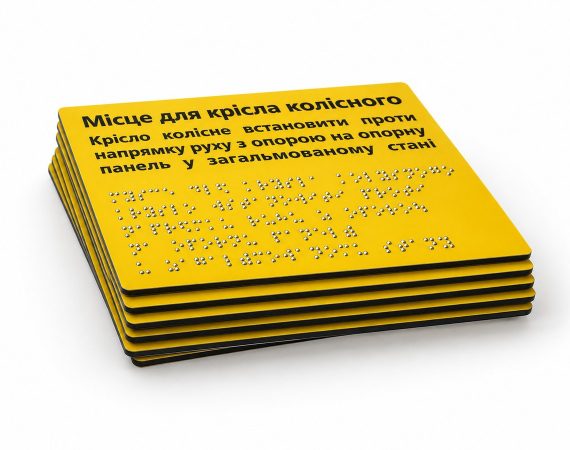 Стос жовтих табличок «Місце для крісла колісного» з написами шрифтом Брайля